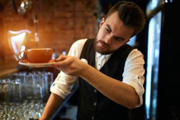 young serious waiter checking a cup of tea before serving it to clients, close up photo