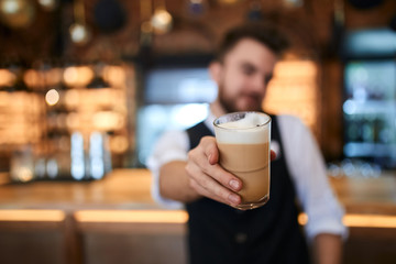 coffee maker giving tasty coffee to visitor in cafe, blurred background, focus on the cup ,take this coffee, man offers to taste beverage