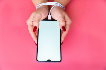 Top view woman hands having a modern smartphone with blank screen on pink background. Addiction on social networking sites, internet and gadgets .