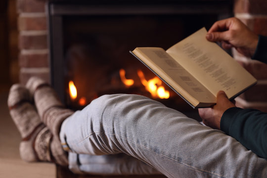 Man reading book near fireplace at home, closeup