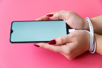 Side view woman hands are having a modern smartphone with empty screen on pink background. Dependences on internet and gadgets