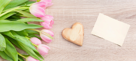 Rosarote Tulpen auf einem hellen Holztisch  mit Holzherz und Postkarte
