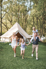 Fototapeta premium Happy Caucasian family, father mother and two little daughters, having fun outdoors in park or camping, enjoying time and laughing together, holding hands and running. Love and parenthood concept