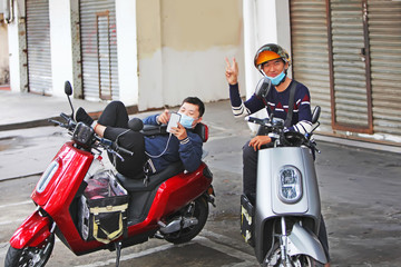 Fototapeta na wymiar Two young Chinese deliver pizza on motorcycles. They have gauze bandages on their faces. Threat of epidemic. Coronavirus 2019.