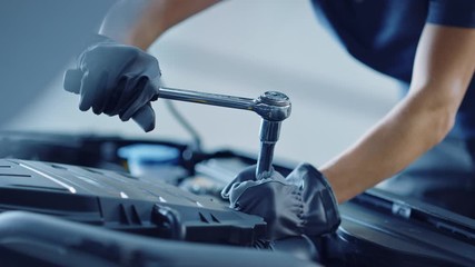 Slow Motion Close Up Footage of a Professional Mechanic Working on Vehicle in Car Service. Engine Specialist Fixing Motor. Repairman is Wearing Gloves and Using a Ratchet. Modern Clean Workshop.  - Powered by Adobe