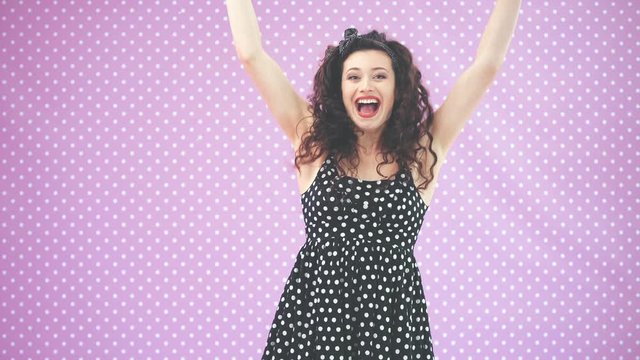 Lovely young girl with kinky hair, in black polka-dots dress bouncing happily, waving her hands, smiling, and crying hurray.