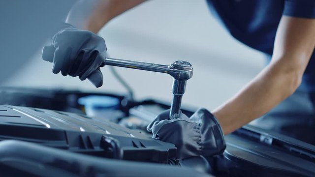 Slow Motion Close Up Footage of a Professional Mechanic Working on Vehicle in Car Service. Engine Specialist Fixing Motor. Repairman is Wearing Gloves and Using a Ratchet. Modern Clean Workshop. 