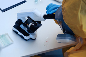 Scientist in chemical protective suit using microscope at table, closeup. Virus research