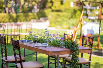 Beautifully decorated wooden table in a summer open-air cafe. Green branch and fresh flowers table decoration