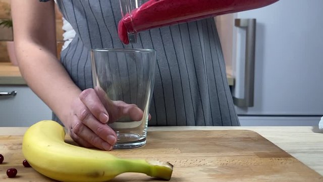 Woman is pouring cranberry banana smoothie into glass