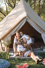 Amazing family day, picnic and camping. Happy family, mother, father and two daughters, sitting in big boho tent wigwam and smiling, embracing each other © sofiko14