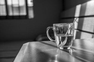 a half-full glass mug on the table with white spoon, monochrome close-up