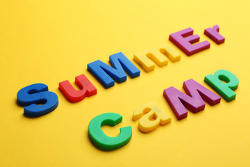 Phrase SUMMER CAMP made with magnet letters on yellow background, closeup