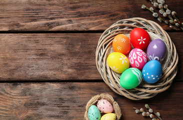 Colorful Easter eggs in decorative nest and willow branches on wooden background, flat lay. Space...