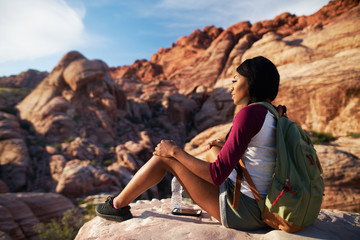 female hiker sitting near cliff ledge at red rock canyon with smart phone and water bottle