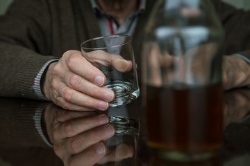 aged man hand holds empty transparent glass sitting at brown table with blurry cognac