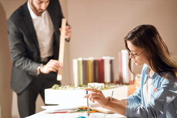 young woman and man working on blueprint, close up cropped side view photo. man in elegant suit holding a ruler in the blurred background