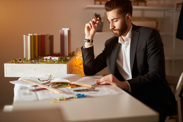 young handsome pensive thoughtful bearded brunette man in elegant black suit holding a pencil in his hand and thinking about development of neighbourhood, close up photo