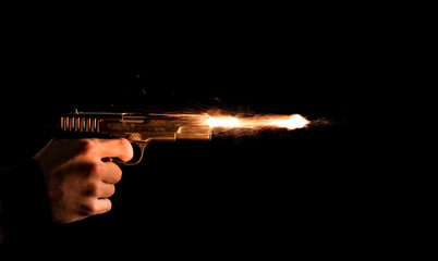 The hand presses the trigger of the gun and the flame from the shot escapes from its muzzle - 329129414