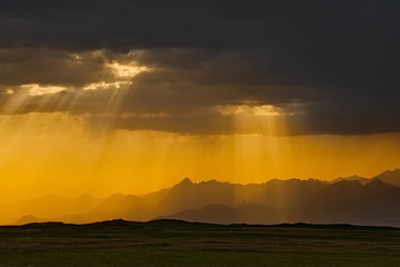 Kyrgyzstan. The sun rays at sunset break through the gloomy rainy clouds