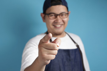 Portrait of young male Asian chef or waiter smiling and pointing forward, looking at camera. Choosing someone concept with selective focus