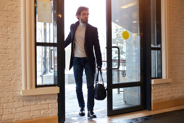 young businessman holding a black leather bag and opening the door of the office, full length photo. strange man thinking about robbery - 329129871