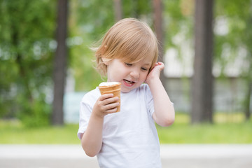 Beautiful baby with blue eyes in white tshirt with glass of vanilla ice cream in hand.