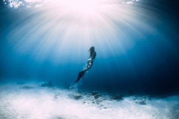 Freediver woman with fins glides over sandy sea bottom in sea. Freediver and amazing light