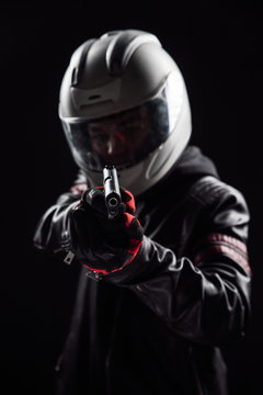 A bandit in a motorcycle helmet and leather jacket with a gun