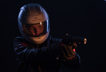 A bandit in a motorcycle helmet and leather jacket with a gun
