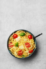Spaghetti with basil and tomato. Italian pasta dish in a bowl viewed from above. Top view. Copy space.