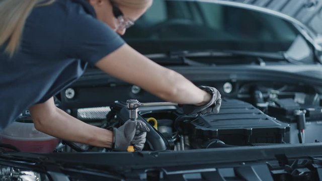 Slow Motion Portrait Footage of a Female Mechanic Working on a Vehicle in a Car Service. Empowering Woman Fixing the Engine. She is Wearing Gloves and Using a Ratchet. Modern Clean Workshop. 