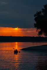 Silhouette of a sailor in a kayak canoe on the lake in the sunset light near an island, Danube...