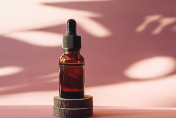 Glass bottle with moisturizing serum on wooden saw cuts on a pink background. Brown bottle with a...