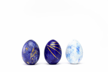 Three easter eggs trendy colored classic blue, white and golden decorated on white table. Happy Easter card with copy space for text. Minimal style.