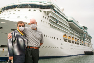 Senior Couple Wearing Face Masks Standing In Front of Passenger Cruise Ship