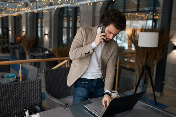 young manager talking on smart phone, texting message on laptop, close up photo. guy serfing, browsing the net, internet