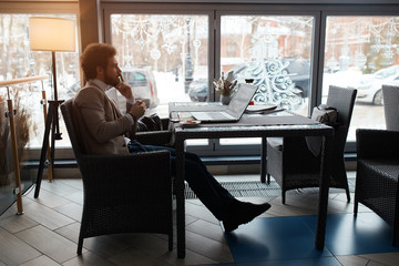 smart businessman sitting on the chair, touching his lips with fingers, trying to overcome problems, making decision, full length side view photo.
