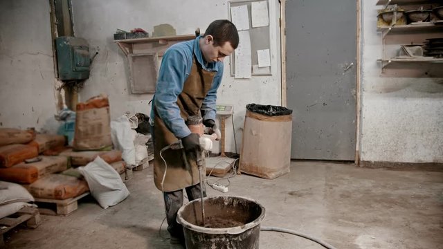 Concrete industry - young man worker mixing concrete out of cement water and pieces of glass using a hand mixer