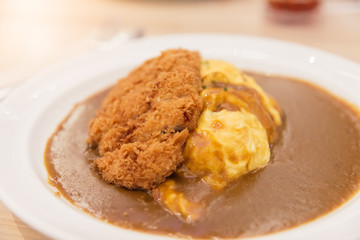 Japanese curry rice with omelet or omurice and deep fried breaded pork cutlet or Tonkatsu on wooden table