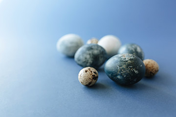 Beautiful group ombre blue Easter eggs with quail eggs and feathers on a blue background. Easter concept. Border eggs. Copy space for text