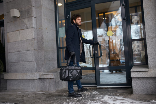 Elegant Stylish Businessman Opens The Door To His Office. Stylish Man In A Coat With A Beard Enters The Building With A Bag In His Hands.full Length Side View Photo