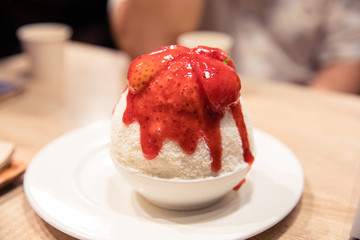 Strawberry Bingsu or shaved ice dessert topped with strawberry sauce and fresh strawberry in white bowl