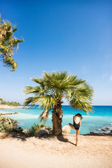 Funny Moment. Woman Standing on One Leg under Palm Tree on Mediterranean Beach.