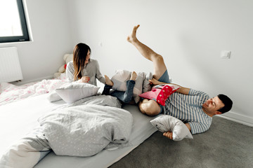 people, family and morning concept - happy child with parents having pillow fight in bed at home,family with a funny pillow fight on the bed. Parents spend their free time with their daughters.