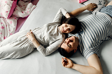 happy young family wakes up early in the morning in bed,top view of a couple who wakes up,husband and wife are smiling and hugging tenderly,peeping on the couple who is on the bed