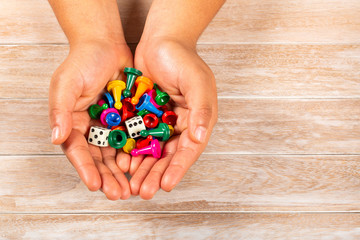 Hands holding game pieces of different colors and dice.