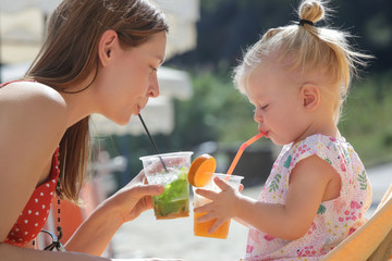 Fototapeta premium Mommy and her toddler girl enjoying a hot summer day at the beach bar, family vacation concept
