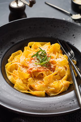 Fettuccine pasta with traditional Italian Passat sauce and parmesan cheese in black plate on dark background. Top view.