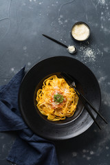 Fettuccine pasta with traditional Italian Passat sauce and parmesan cheese in black plate on dark background. Top view.